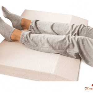 Ein weißes, breites Stützkissen. Darauf liegen die Beine eines Menschen. Es wird zur Vorbeugung von Fersen-Dekubitus eingesetzt.